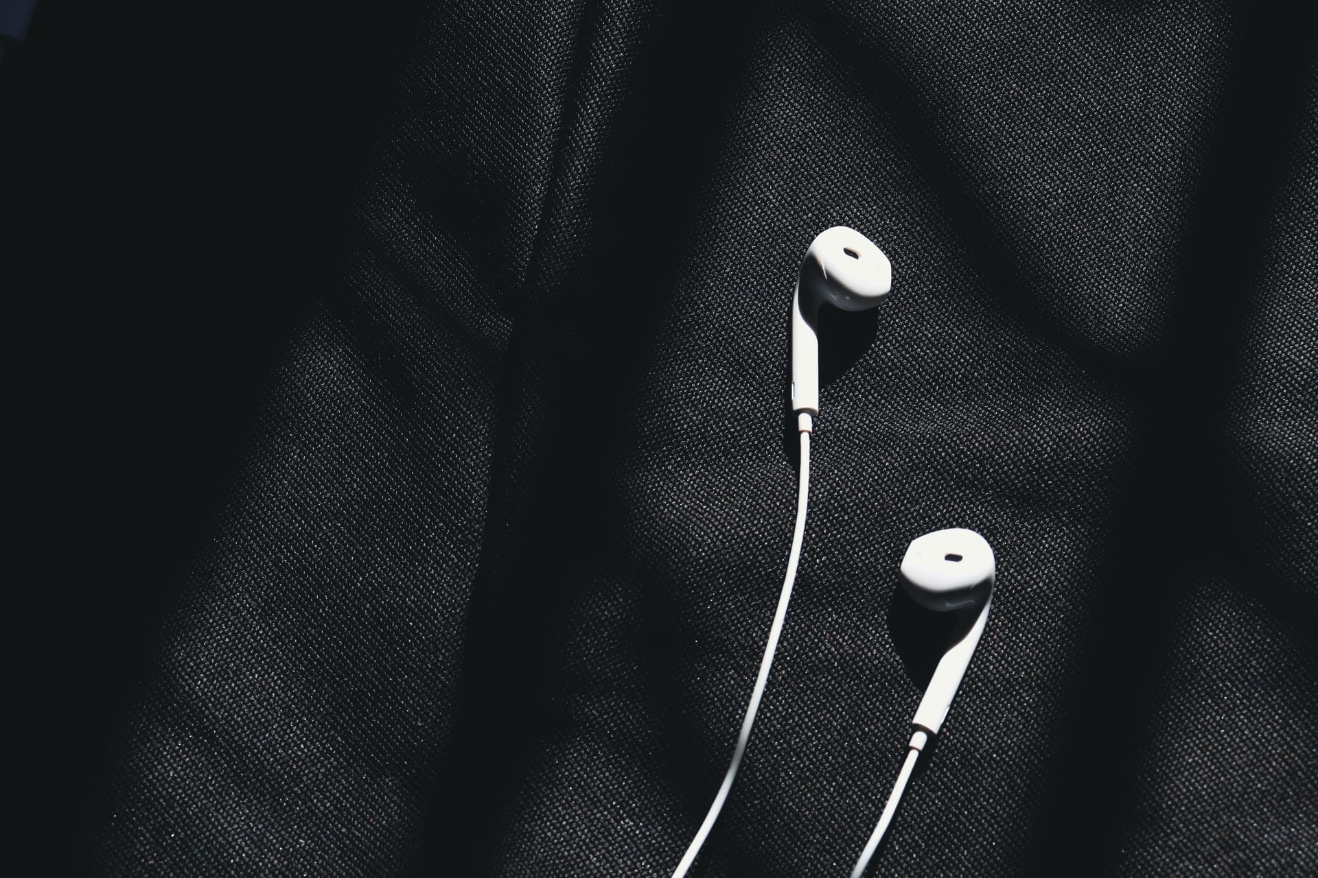 An earpiece and its cable coiled on dark suiting fabric.