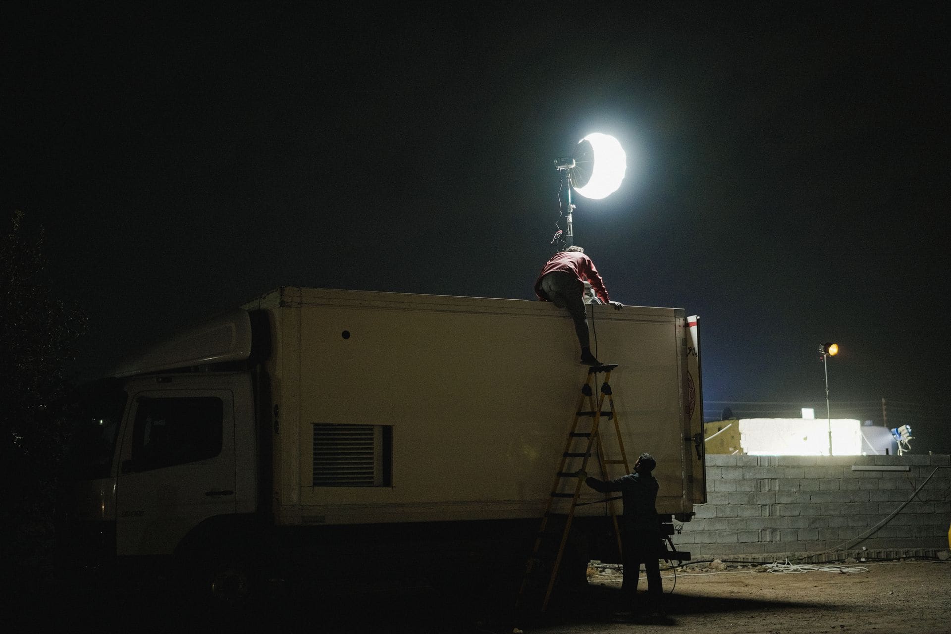 A film crew rigging a balloon light above a unit truck on a night shoot.