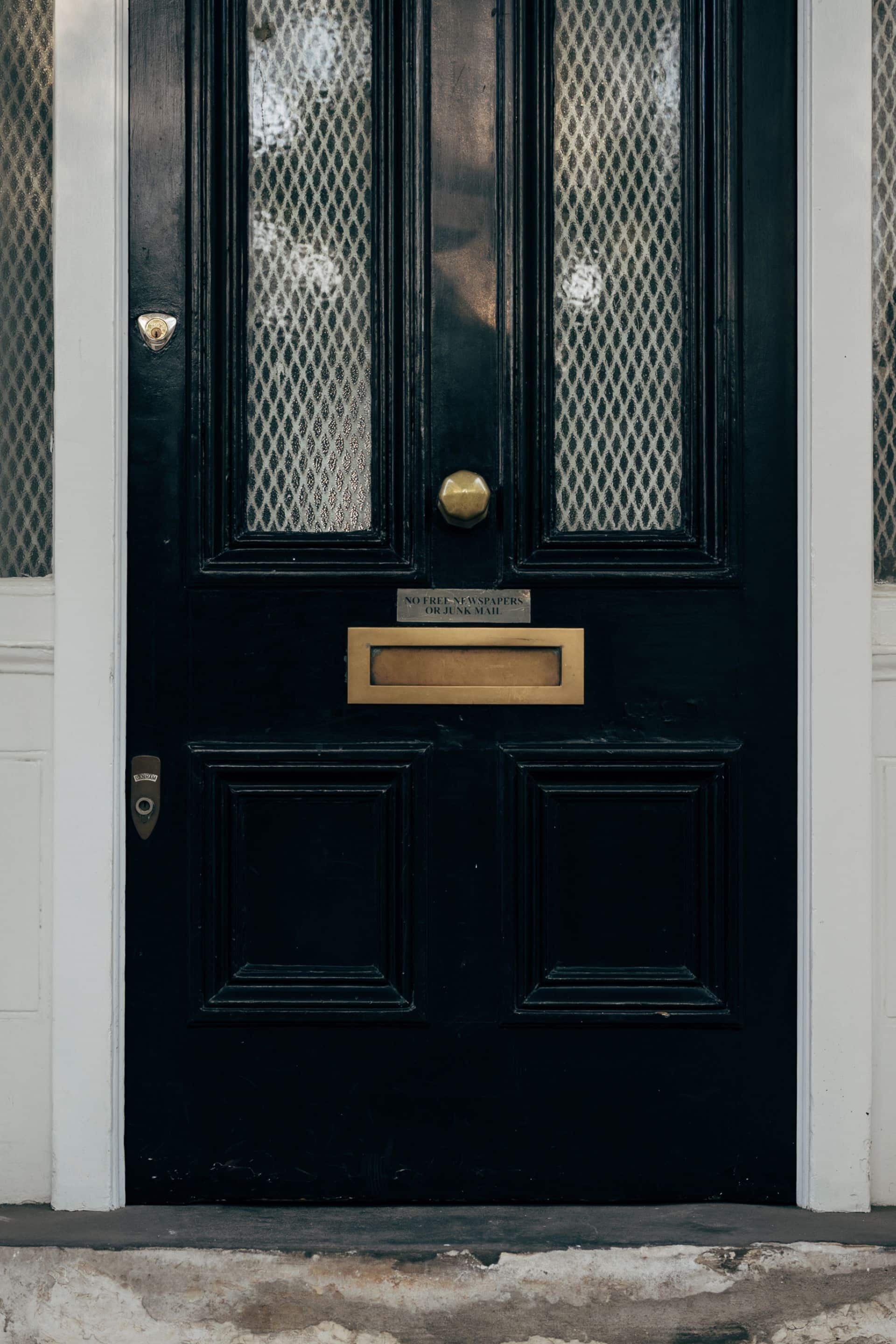 A glossy black London front door with a brass letterbox, framed by white columns.