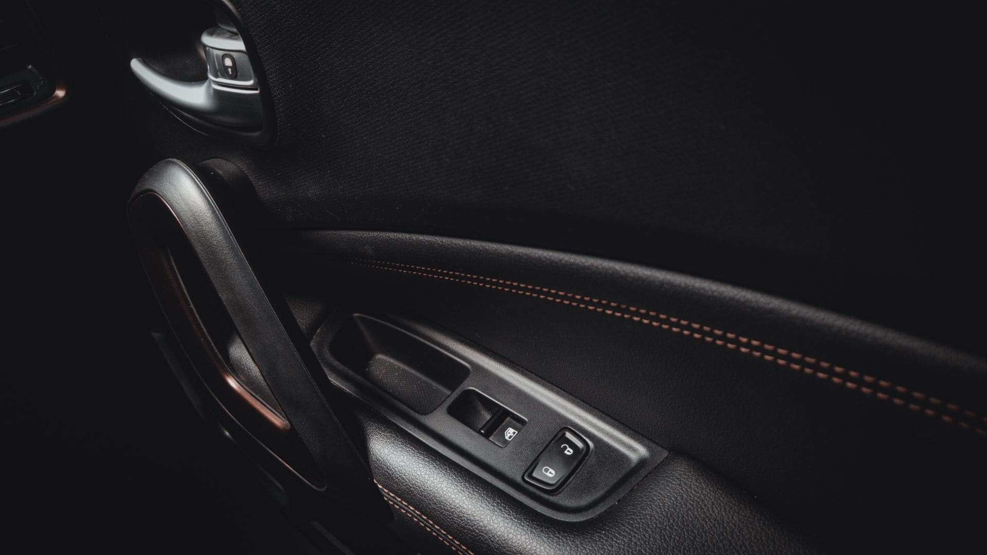 A stitched leather door pull inside a dark car interior.
