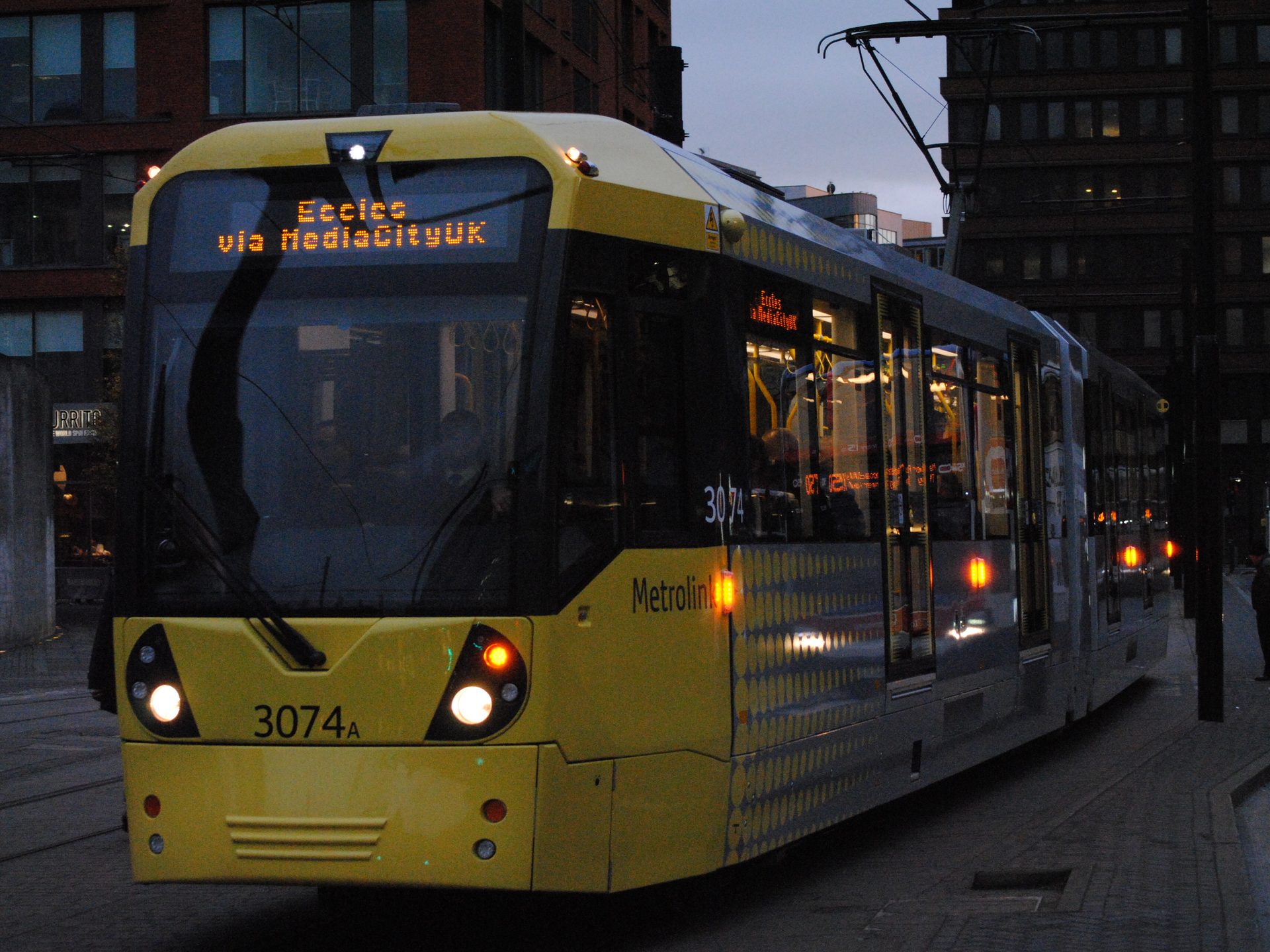 A Metrolink tram waiting in central Manchester after dark.