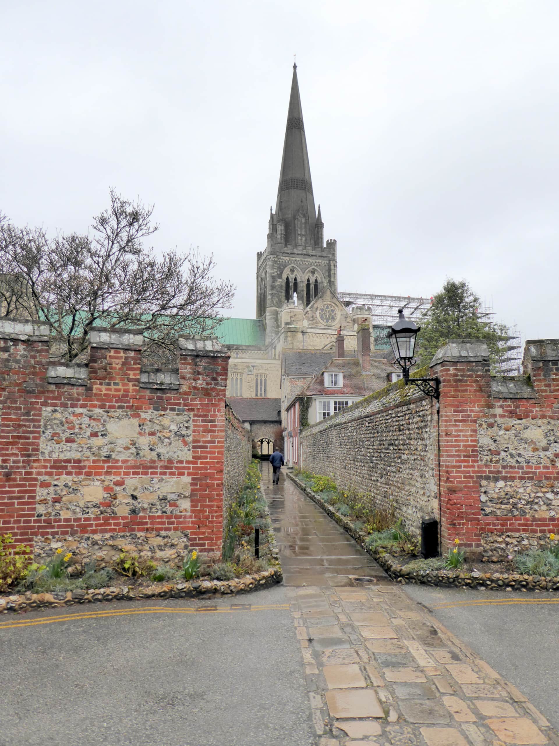 A flint-walled lane leading toward Chichester Cathedral's spire.